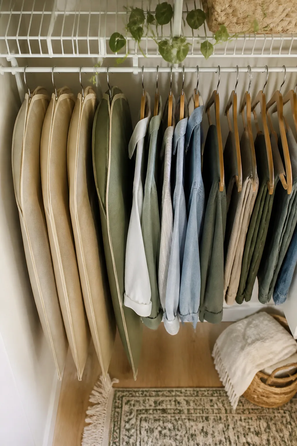 Several garment bags hanging together at one end of a closet rod, separated from everyday shirts and pants.