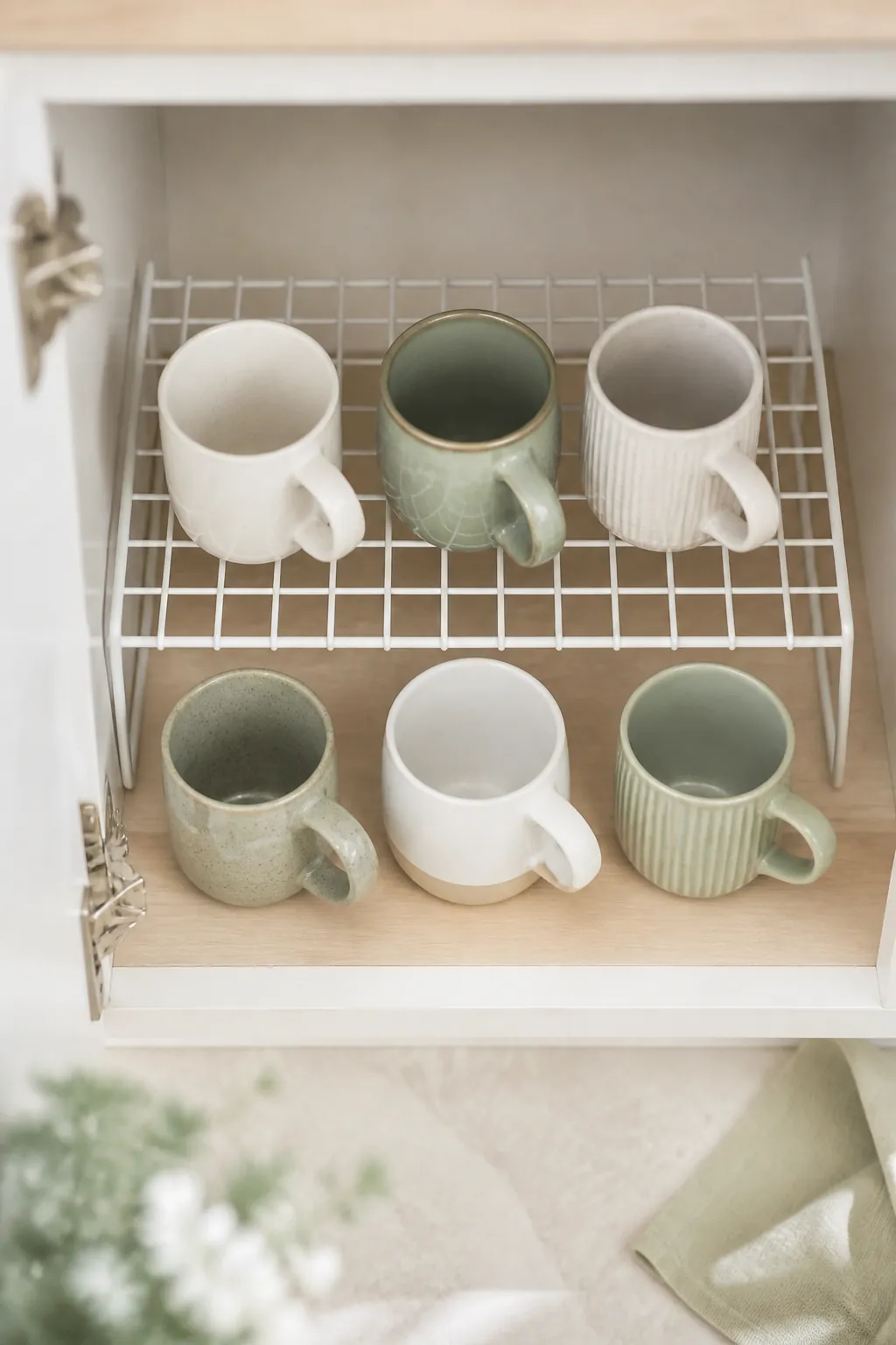 Mugs stored on two levels of a wire shelf riser inside a kitchen cabinet, doubling the usable height