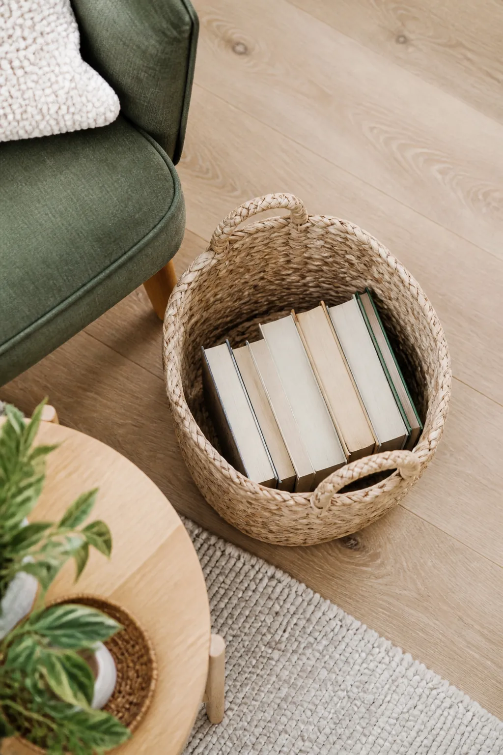 A woven basket on the floor beside an armchair holding several paperback books standing upright inside it.