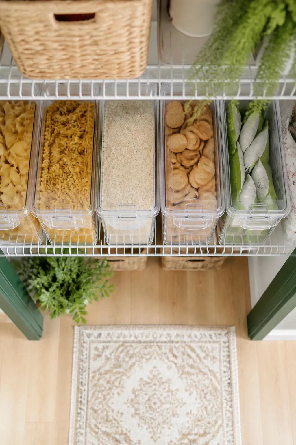 Clear lidded pantry bins of pasta, rice and snacks lined up on a wire shelf inside a closet, each with a small label