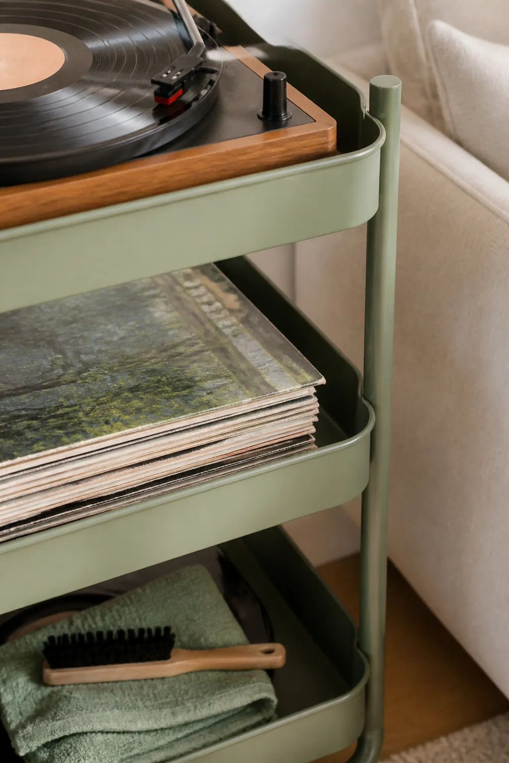 A turntable on top of a rolling cart, with records on the middle shelf and cleaning supplies on the bottom.