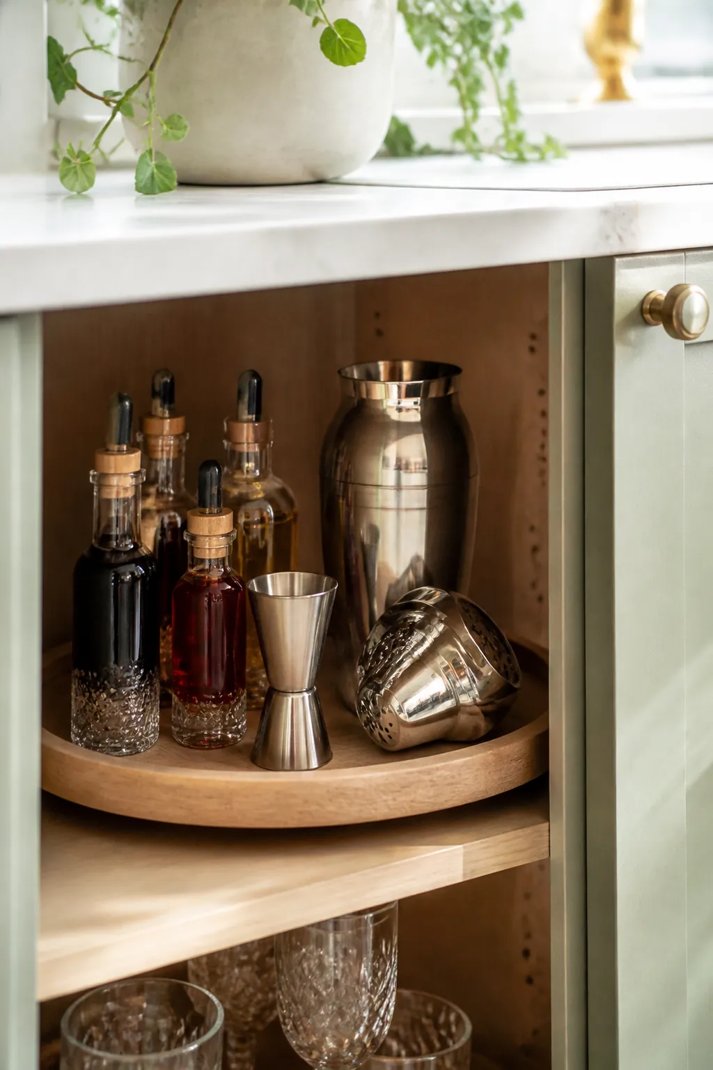 A round turntable in a corner cabinet holds syrup bottles, bitters, a jigger, and shaker parts.